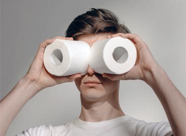 A person holding two rolls of toilet paper over their eyes.