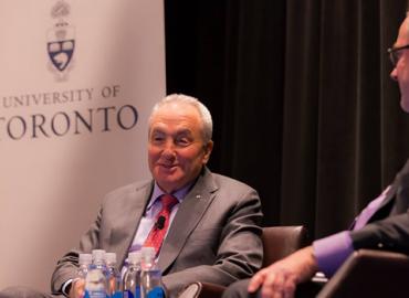 Lorne Michaels sitting in front of a banner with the University of Toronto logo on it