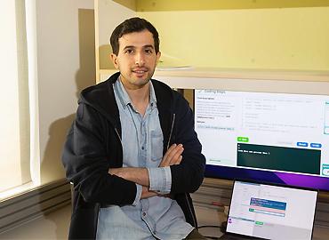 Majeed Kazemitabaar sitting on a desk with a computer screen behind him