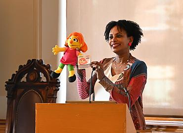 Professor McEwen behind a podium holding up the Julia puppet