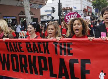 Women marching while holding a banner that says &amp;quot;Take back the workplace.&amp;quot;