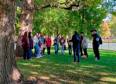 Alan Ackerman’s class stands outside under beautiful lush green elm trees.