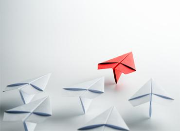 Multiple white paper airplanes and one red paper airplane.