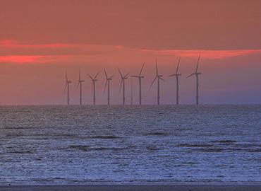 Several wind turbines in the ocean at sunset