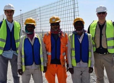 Adam Sheikh and construction workers, standing in the sun, wearing cooling vests in Qatar