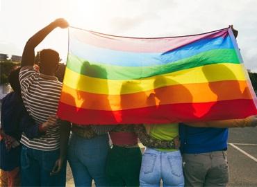 Young diverse people having fun holding LGBT rainbow flag outdoor 