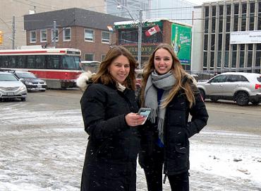 Shauna Brail, director and associate professor, teaching stream in the Urban Studies Program at Innis College with second-year student Monica Brondholt standing on the side of a busy street with cars and a streetcar in the background.