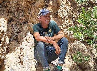 Sarah Murray sitting on a rocky outcropping in a T-Shirt and baseball hat