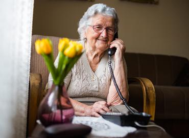 An elderly person on the phone smiling.