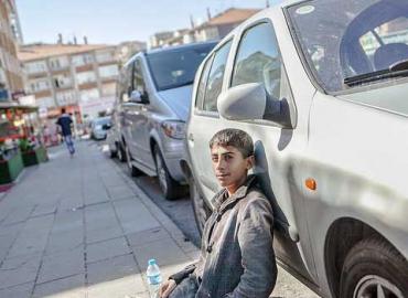 A young Syrian refugee sits on the sidewalk and leans against a car in Ankara, Turkey