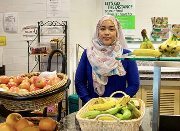 Tammara Soma standing in front of baskets full of bananas, apples and oranges