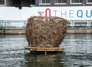 A large structure of twine on a dock in the middle of a harbor.