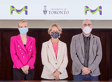 3 masked people standing behind a long desk with a U of T sign behind them