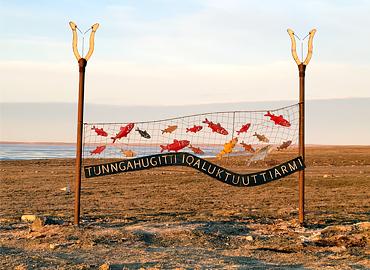 An outdoor sign featuring fish and the name in Inuinnaqtun which means a “good fishing place.”