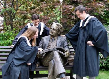 Victoria graduates pose with a statue of Northrop Frye on Victoria College&amp;#039;s campus