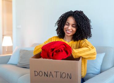 A person putting clothes in a box that says &amp;quot;donation&amp;quot;.