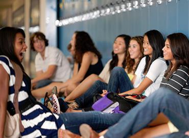 Group of female students sitting by lockers, smiling and chatting.
