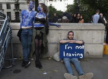 Young man sitting on the ground with a blue sign reading, &amp;quot;I&amp;#039;m not leaving&amp;quot;.