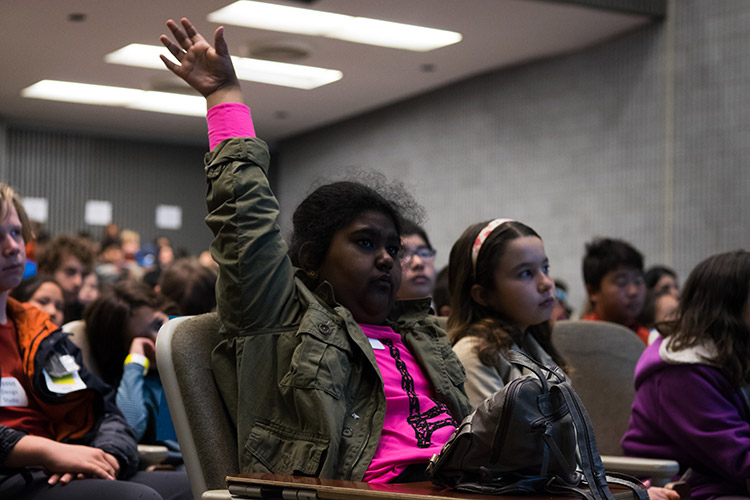A young person raises their hand to ask a question. 