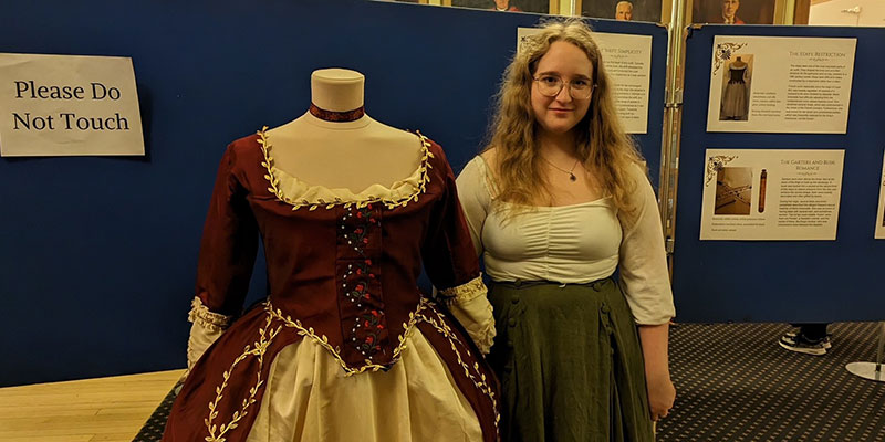 Tara Downie standing beside an old Victorian style red dress.