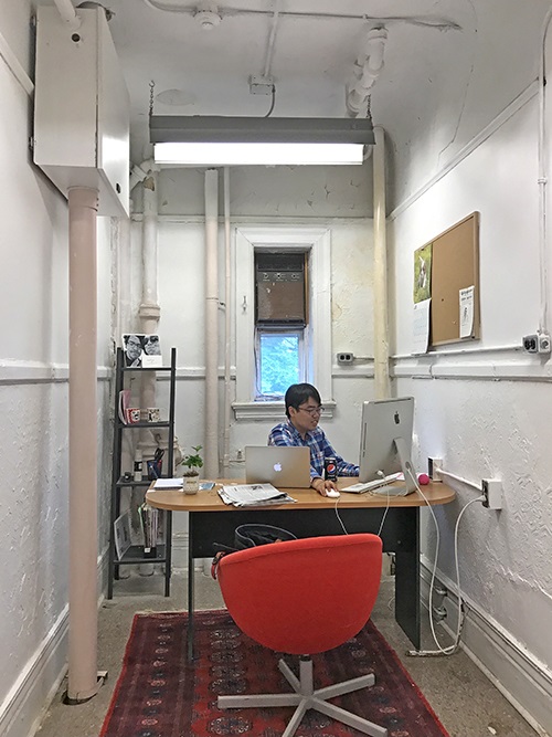Tom Yun at his desk - the small room looks unfinished - has exposed pipes