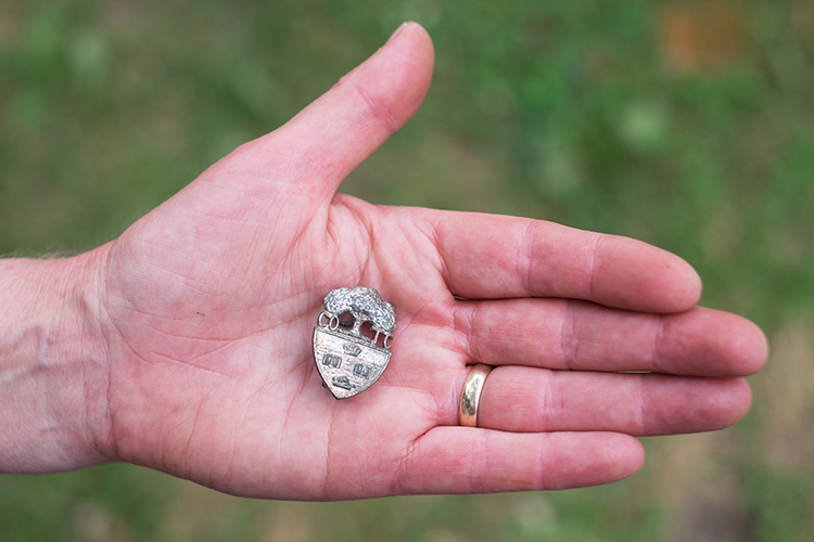 A hand holding a pin with the U of T crest associated with the local Canadian Officers’ Training Corps.