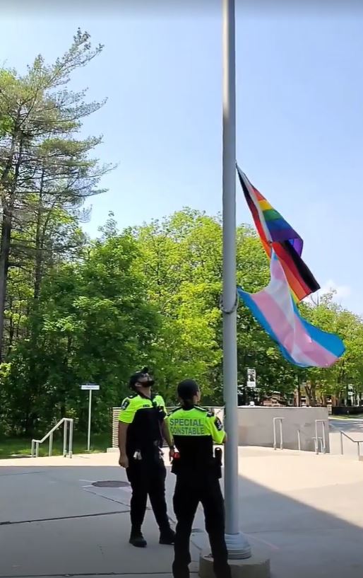two U of T special constables raising the Pride and Trans flags up a flag pole
