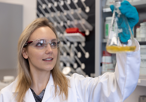 Virlana Shchuka holding a beaker with liquid in a lab.