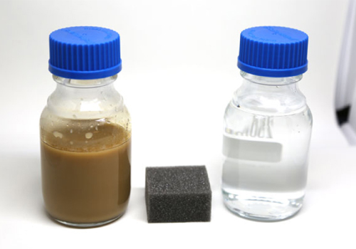 Two containers, one filled with clear water, the other with brown water, a sponge in the middle.