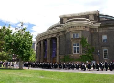 A group of new graduates walk into convocation hall on a sunny June day.