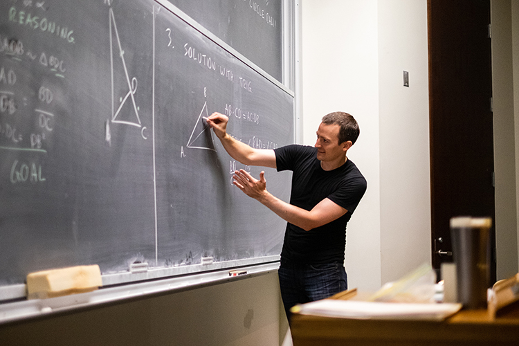 Zack Wolske writes problems on the blackboard